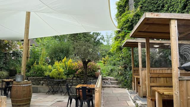 Outdoor dining area with wooden tables, chairs, and a large white canopy, surrounded by lush greenery and flowers.