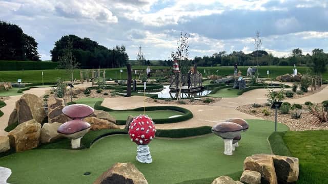 Colorful mini-golf course featuring whimsical mushrooms, rocks, and a pond, with players enjoying the game under a cloudy sky.
