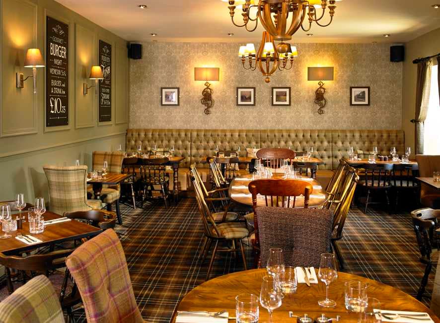 Elegant restaurant interior featuring wooden tables, upholstered seating, and decorative wall sconces in a cozy atmosphere.