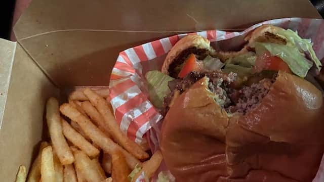 A takeout box containing a half-eaten burger with lettuce and tomato, alongside a serving of fries.