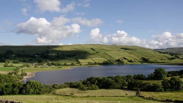 Serene landscape of Semerwater lake surrounded by lush green hills and scattered trees under a blue sky with clouds.
