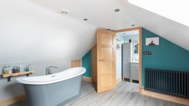 Modern bathroom with a freestanding bathtub, wooden accents, teal walls, and a stylish radiator.