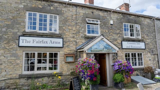 Stone building with large windows, colorful flower baskets, and signs for "The Fairfax Arms" and "Country Inn and Restaurant."