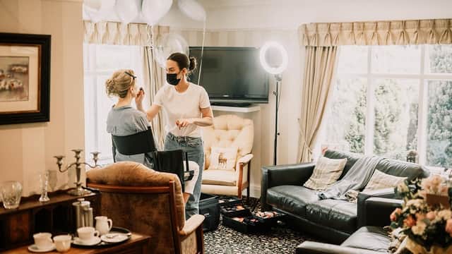 A salon interior with a stylist applying makeup to a client, surrounded by elegant furniture and balloons.