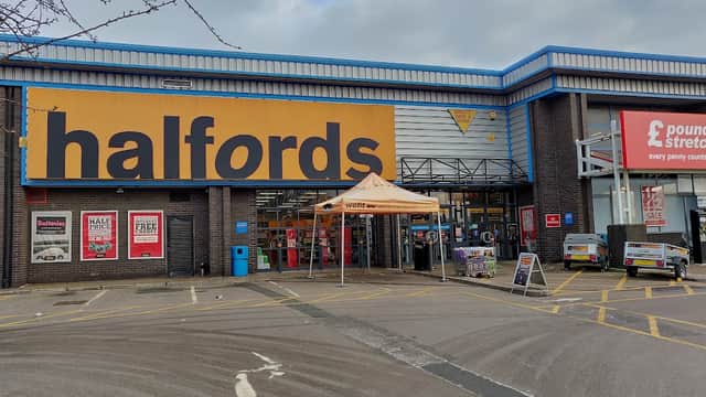 Halfords store entrance with large signage, orange canopy, and parking area in Dewsbury, Yorkshire.