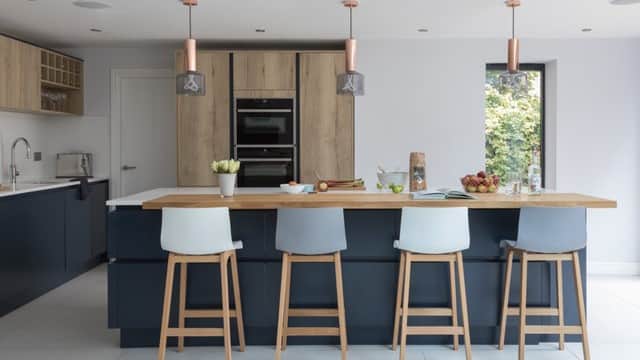 Modern kitchen with a wooden island, bar stools, sleek cabinetry, and pendant lights, featuring fresh fruits and decor.