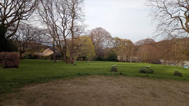 Lush green park with bare trees, a few bushes, and a distant house under a cloudy sky in Meltham, Yorkshire.