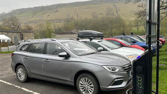 Pod Point charging station with a gray car parked nearby, surrounded by other vehicles and a hilly landscape in Kettlewell.