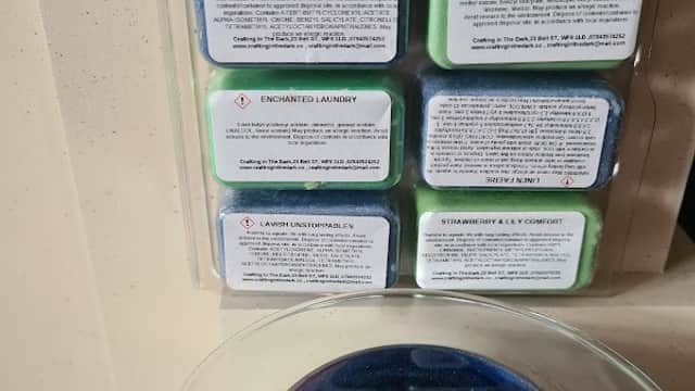 Wax melts in various colors and scents displayed on a wall, with a glass container below filled with colorful beads.