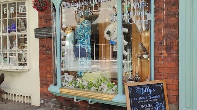 Charming gift shop with a decorative window display, featuring plants, clothing, and a menu board outside.