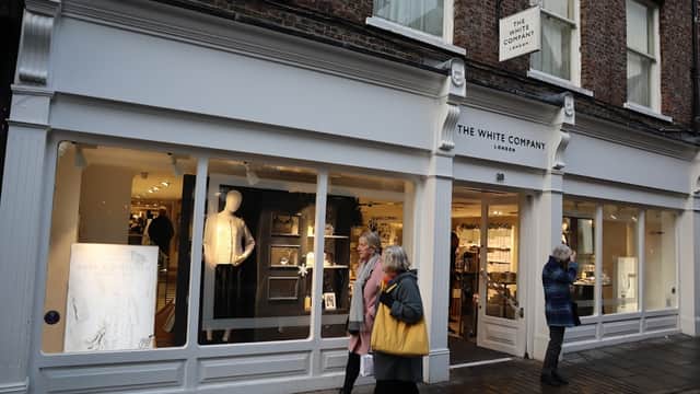 The White Company storefront featuring elegant displays, mannequins, and shoppers in a charming street setting.