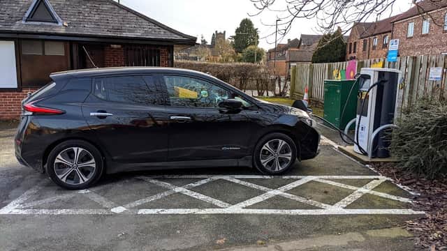 Black electric car parked at a bp pulse charging station in Minskip, Yorkshire, with buildings and trees in the background.