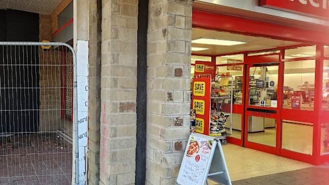 Entrance to Batley Shopping Centre with a signboard and safety notices. Red and white decor visible.