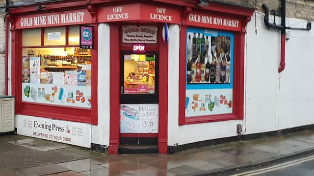 Gold Mine Mini Market storefront with red trim, displaying various beverages and snacks, and an "Open" sign.