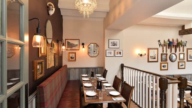 Cozy dining area with wooden tables, plaid seating, framed photos, and a chandelier in a charming B&B.