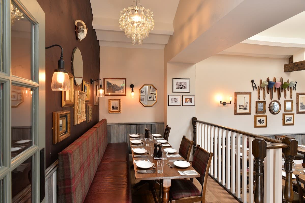 Cozy dining area with wooden tables, plaid seating, framed photos, and a chandelier in a charming B&B.