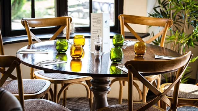 A wooden dining table set with colorful glassware and cutlery, surrounded by wooden chairs in a cozy restaurant setting.