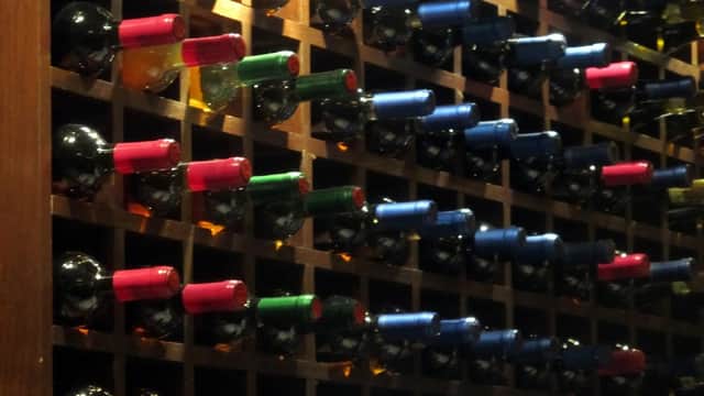 Rows of wine bottles in a wooden rack, featuring various colored caps including red, blue, and green.
