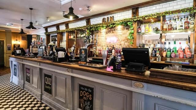 A stylish bar with a wooden counter, colorful liquor bottles, and a checkered floor in a cozy setting.