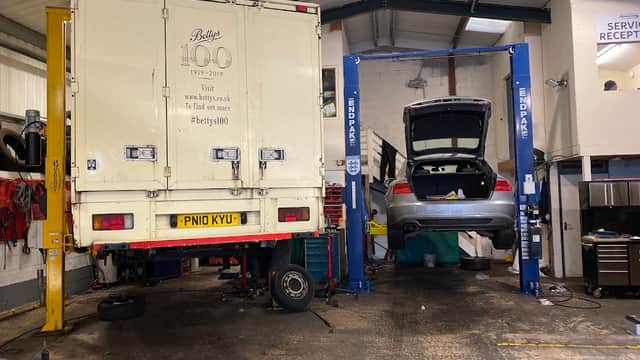 Two vehicles on lifts in a garage, one a truck and the other a car, with tools and equipment visible in the background.