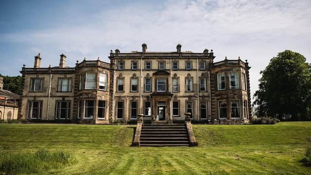 Grand stone building with multiple windows, steps leading to the entrance, surrounded by a green lawn and trees.