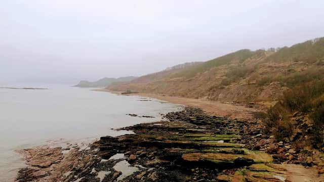 Rocky shoreline with gentle waves, cliffs in the background, and a cloudy sky at Cayton Bay, Scarborough.