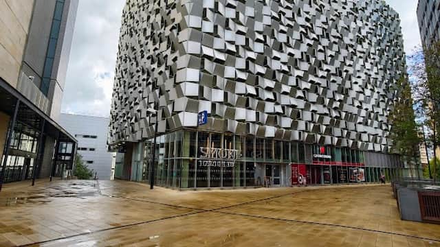 Modern architectural building with a textured facade, surrounded by wet pavement and a cloudy sky in Sheffield.