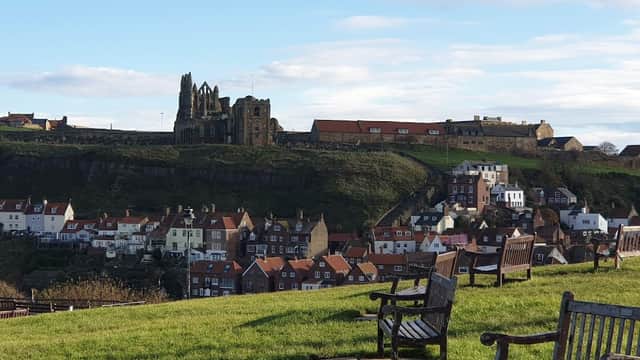 View of Whitby with benches in foreground, showcasing rooftops and the historic abbey on the cliff.