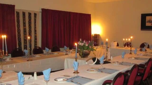 Elegant dining setup with blue napkins, candles, and floral centerpiece in a warmly lit hall. Red curtains in the background.