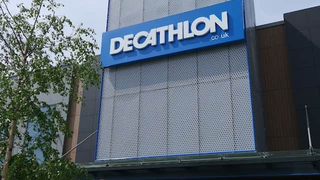 Decathlon store exterior in Sheffield with large blue signage and modern architectural design. Green plants in foreground.