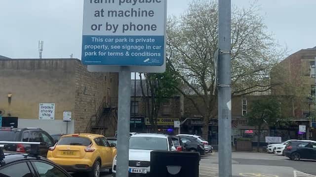 Sign indicating parking fees at Wellington House Private Car Park with vehicles and trees in the background.