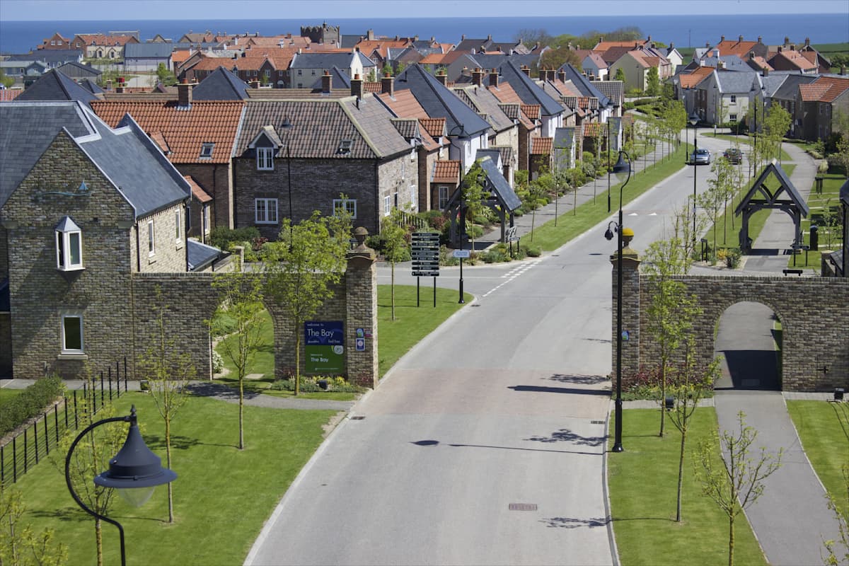 Quaint residential area in The Bay Filey, featuring stone houses, manicured lawns, and a clear blue sky.