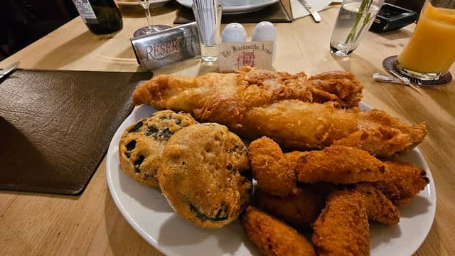 Plate of fish and chips with crispy batter, alongside two cookies and chicken nuggets on a wooden table.