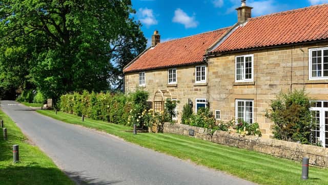 Charming stone building with red roof, surrounded by greenery, along a quiet road in North Yorkshire. Bright blue sky.