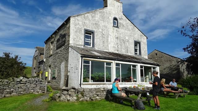 The Old Hill Inn, a stone building with large windows, surrounded by green grass and picnic tables, under a blue sky.