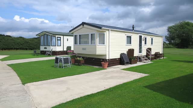 Two static caravans on a grassy campsite, with a concrete path and cloudy sky in the background.