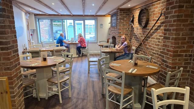 Cozy restaurant interior with wooden tables, chairs, brick walls, and customers dining by the window.