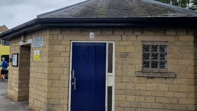 Public toilets in a stone building with a blue door, surrounded by a paved area and trees in Pickering, Yorkshire.