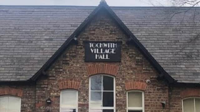 Tockwith Village Hall features a brick facade, large windows, and a yellow recycling bin in the foreground.