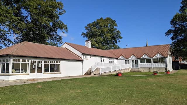 Snainton Village Hall features a white exterior, large windows, a sloping roof, and a green lawn surrounded by trees.