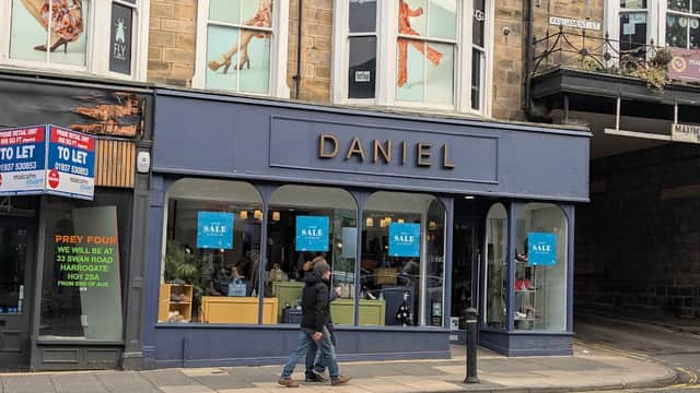 Shoe shop with large windows displaying footwear, sale signs, and a person walking by on a street in Harrogate.