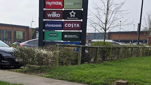 Sign for St. James Retail Park with store names like M&S, Aldi, and Costa, surrounded by greenery and parked cars.