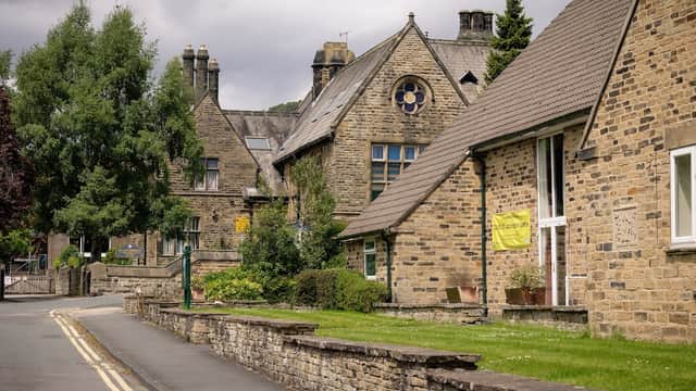 Historic stone buildings line a quiet street, with green trees and a memorial hall featuring a round window.