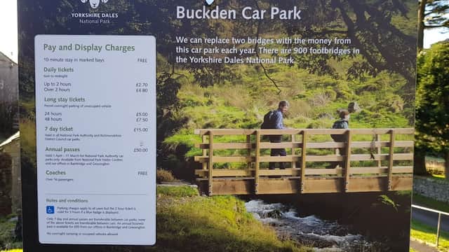 Welcome sign for Buckden Car Park, featuring a scenic bridge and information on parking fees and annual passes.