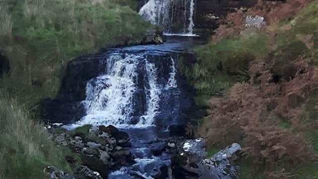 Waterfall cascading down rocky terrain, surrounded by lush greenery and autumn foliage in Cotterdale, Yorkshire.