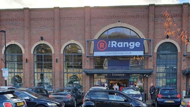 Brick building with large arched windows, featuring a prominent sign for "The Range" and parked cars in front.