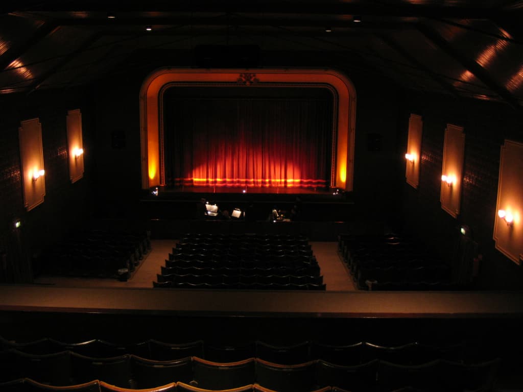 Interior of Pendle Hippodrome Theatre featuring a stage with red curtains and rows of empty seats.