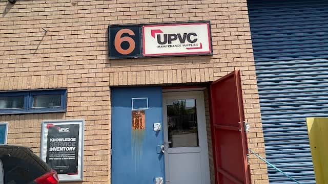 Sign for UPVC Maintenance Supplies on a brick building with a blue door and a red open door, surrounded by a paved area.