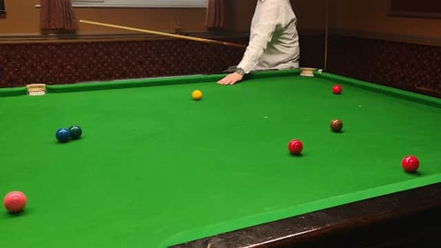 A man in a white shirt stands at a snooker table with colorful balls arranged on a green felt surface.