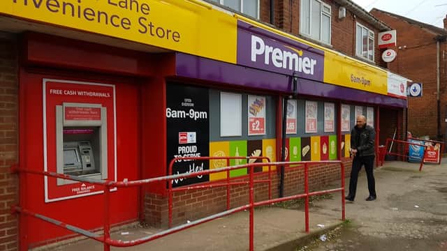 Premier Off Licence storefront with bright signage, ATM, and a man walking by in Leeds, Yorkshire.